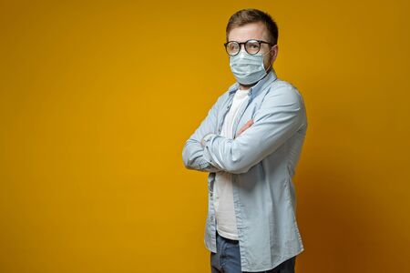 Calm man in a medical mask and glasses, standing with arms crossed and looking at the camera, with copy space.の写真素材