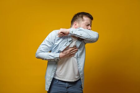 Ðan coughs in his elbow and holds hand on chest, experiencing pain. Correct sneezing. Concept of spread of the virus.の写真素材
