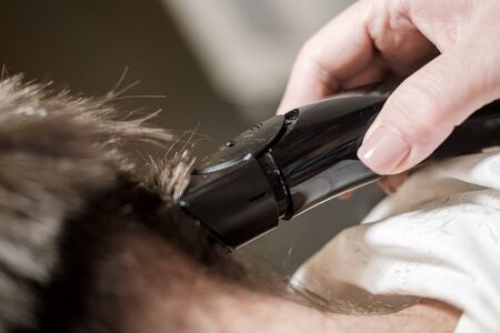 Female hand does cut hair on a mans head with a trimmer. Getting groomed.の写真素材