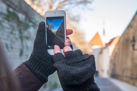 Female hands in mittens photograph on the smartphone beautiful sights of the old city, on a sunny, winter day. Tallinn, Estonia.の写真素材
