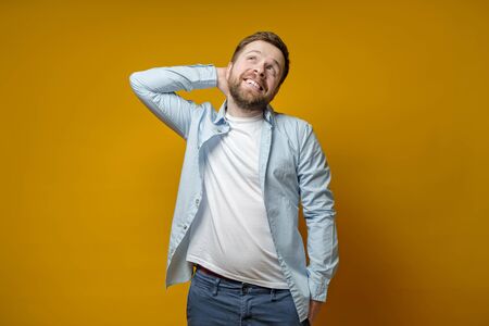 Happy, in love bearded Caucasian man smiles and looks dreamily upstairs, holding hand behind head.の写真素材