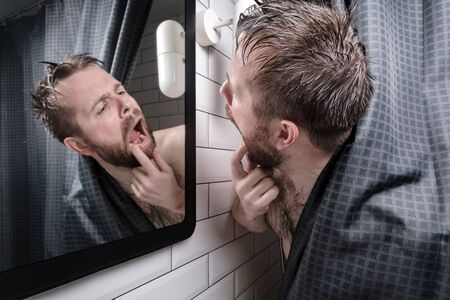 Excited, frustrated man and carefully examined his teeth in the mirror, peering out from behind the curtains in shower.の写真素材