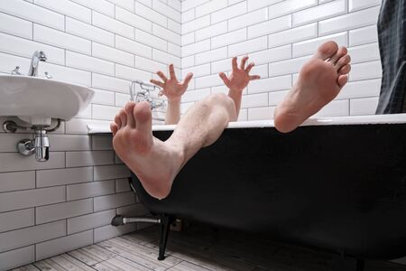 Wet male legs and hands with spread fingers are visible from the cast-iron bathtub in the modern bathroom interior.の写真素材