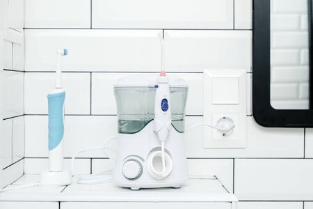 Electric oral irrigator and a rechargeable toothbrush are in the white tiled bathroom, next to the mirror. Close-up.の写真素材