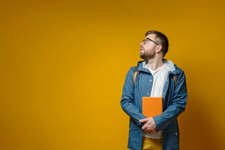 Attractive student with a book in hands looks bewildered to the side, with copy space, on a yellow background. Education concept.の写真素材