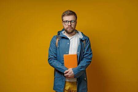 Attractive student or young scientist is standing with a book in hands, in a raincoat and calmly looking at the camera.の写真素材