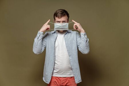 Man with a serious look, puts on a medical mask, to protect against a dangerous virus, on a green background. Health concept.の写真素材