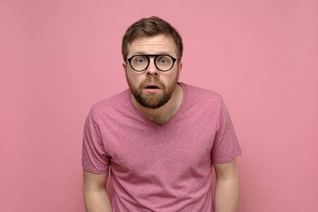 Man with glasses is confused, he leaned forward, looks with a shocked expression on his face and does not believe what he saw.の写真素材