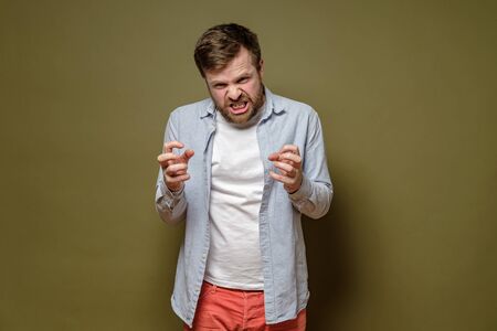 Frenzied, bearded man, clenches fists in fury and grins teeth angrily. Isolated, on a green background.の写真素材