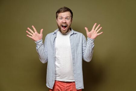 Bearded man is delighted, he screams with happiness and makes a gesture with hands, on a green background.の写真素材