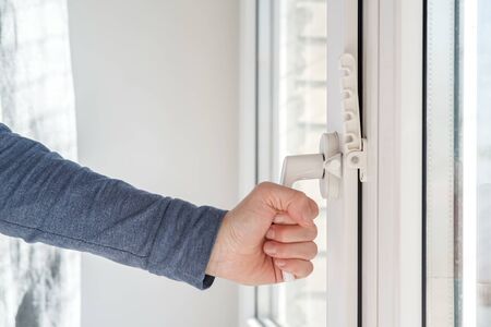 Female hand closed a modern white PVC window, with an attached fixing device for ventilation, in natural light.の写真素材