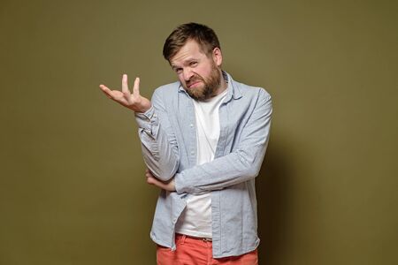 Caucasian man with a doubtful expression on face shrugs, makes a hand gesture and an uncertain grimace, on a green background.の写真素材