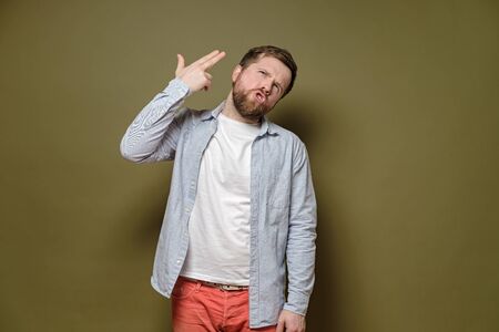 Man pointing finger at head, as if it were a gun and was going to shoot himself with the emotional expression. Stress concept.の写真素材
