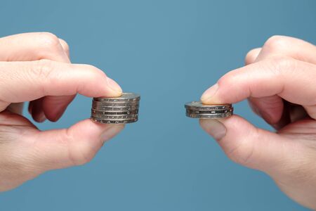 Hands are comparing two stacks of coins of different sizes, indicating a worsening financial situation. Economic concept. Close-up.の写真素材