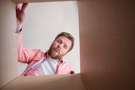 Surprised, pleased bearded man unpacks a delivered box with a parcel or a gift. Unboxing inside view. Copy space.の写真素材