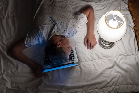 A tired woman with a laptop overworked, working remotely at home, and lay on the keyboard as a pillow on quarantine self-isolation during an epidemicの写真素材