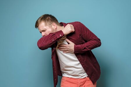 Caucasian man coughs at the elbow and holds hand on chest, experiencing pain. Concept of the spread of a dangerous virus.の写真素材