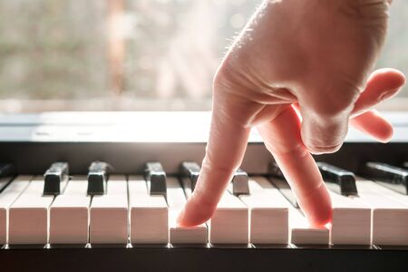 Fingers press the keys of the piano, as if legs were walking, in natural light from the window.の写真素材