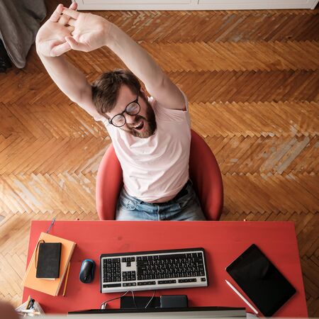 Man is resting, yawns and stretches, working remotely on his computer at home. Concept of quarantine during a virus outbreak.の写真素材