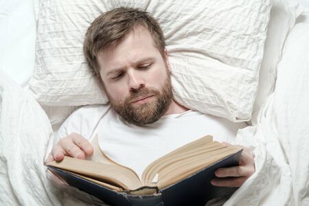 Attractive bearded man reading a book while lying in bed. Education concept. Top view.の写真素材