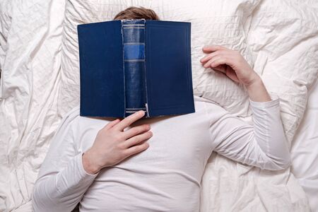 Man in his pajamas fell asleep reading and the book covered his face. Education concept. Top view.の写真素材