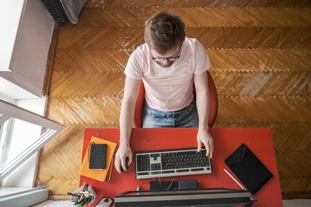 Focused man works remotely at home on a computer. Concept of self-isolation during an outbreak of a viral epidemic and pandemic.の写真素材