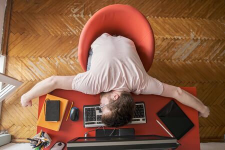 Man sleeps on a keyboard, he works remotely at home on a computer. Concept of self-isolation during a pandemic. Modern lifestyle.の写真素材