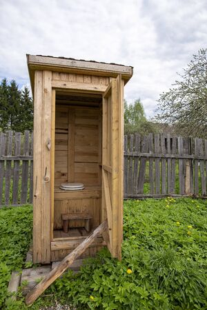 Tradition, wooden, rustic restroom, WC, with a modern toilet seat with a lid, in the yard, against the background of an old fence.の写真素材