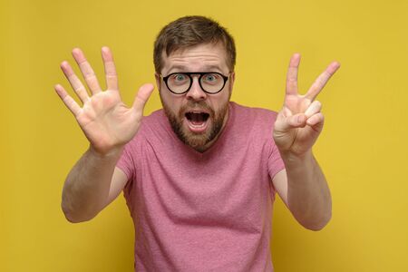 Joyful, emotional bearded man with glasses, shows with his fingers number seven, on a yellow background. Sign 7の写真素材