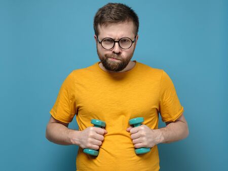 Funny bearded man with overweight decided to go in for sports, took dumbbells in his hands and is ready for training.の写真素材