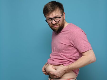 Upset man shows and holds with hands his excess fat on his stomach. Copy space. Overweight person. Healthy lifestyle concept.の写真素材