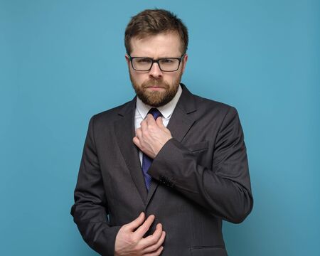 Strict, confident business man straightens his tie and with piercing eyes looks into the camera, on a blue background.の写真素材