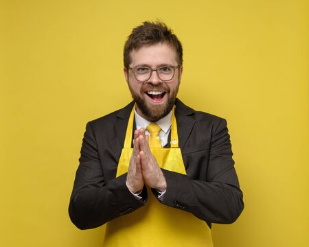 Business man in a suit and apron successfully made a deal, he rejoices, rubs his palms and looks into the camera with happy eyes. Isolated on a yellow background.の写真素材