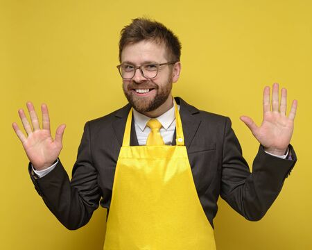 Strange, charming business man in a black suit and yellow apron, made a good deal, he rejoices, smiles and raises palms up.の写真素材