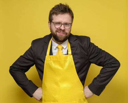 Strange man in a black suit and yellow apron is standing and holding hands on hips and amusingly stares with narrowed eyes.の写真素材