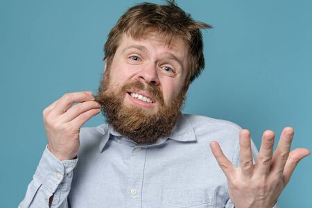 Man is dissatisfied with his shaggy hair and beard, he urgently needs a barbershop. Concept of quarantine during a viral epidemic.の写真素材