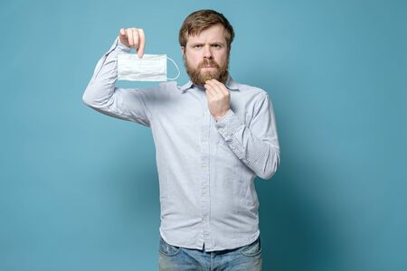 Caucasian man is displeased because a shaggy beard will create problems when wearing a medical mask. Quarantine concept.の写真素材