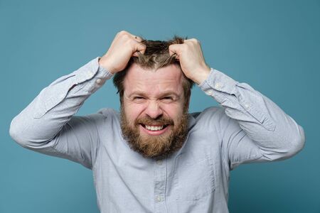 Man is angry and experiencing stress, he furiously rips out his hair and grins. Concept of mental health.の写真素材