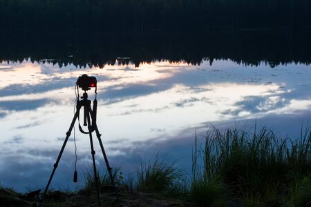 Camera on a tripod on the shore of a forest lake, takes a picturesque night landscape.の写真素材
