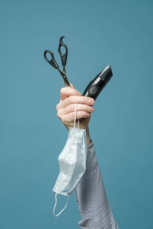 Male hand holds scissors, trimmer and medical mask. Concept of quarantine and the inability to visit a barbershop. Vertical photo.の写真素材