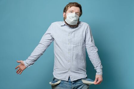No money. Man in a medical mask with empty pockets and a questioning look. Concept of unemployment and crisis due to the pandemic.の写真素材