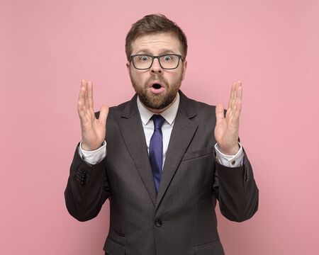 Amazed man in a suit in shock, he makes a gesture with hands and looks in surprise at the camera.の写真素材
