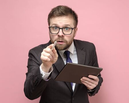 Caucasian businessman in a suit with a tablet looks inquiringly and shows with a stylus to the camera.の写真素材