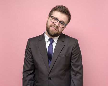 Tired bearded Caucasian man with glasses and a suit smiles mockingly and looks at the camera with indifference.の写真素材