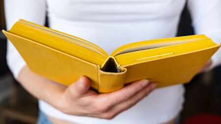 Open thick, old yellow book is held by female hands, on a blurred background.の写真素材