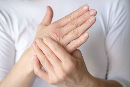 Woman experiences pain in her hand and is massaging a sore spot against a white tee-shirt.の写真素材