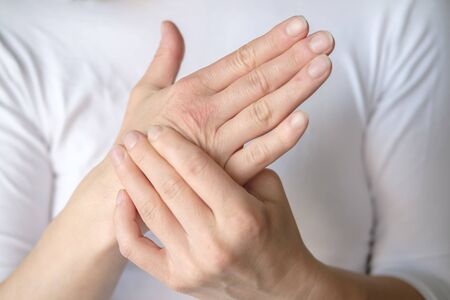 Woman experiences pain in her hand and is massaging a sore spot against a white tee-shirt.