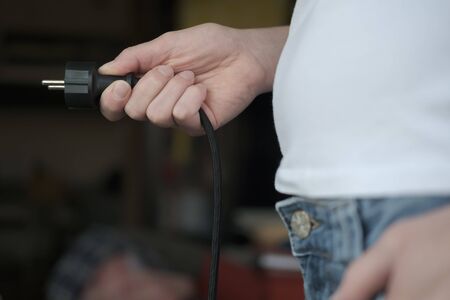 Electric plug with a cord in hand, on a blurred background.の写真素材