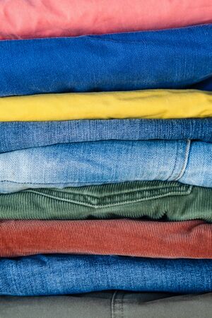 Stack of neatly folded jeans and trousers in bright colors. Abstract background.の写真素材