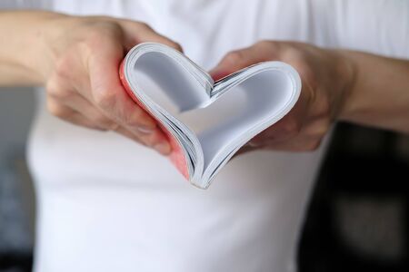 Heart is a symbol of love made of bent sheets of a notebook, female hands are holding near the chest. Valentines Day.の写真素材